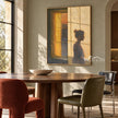 Quiet Figure beside an Amber Window Wall Art shown above a dining table.