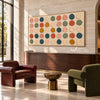 Wide Multicolor Painted Dot Grid Wall Art shown above a wood cabinet between lounge chairs.